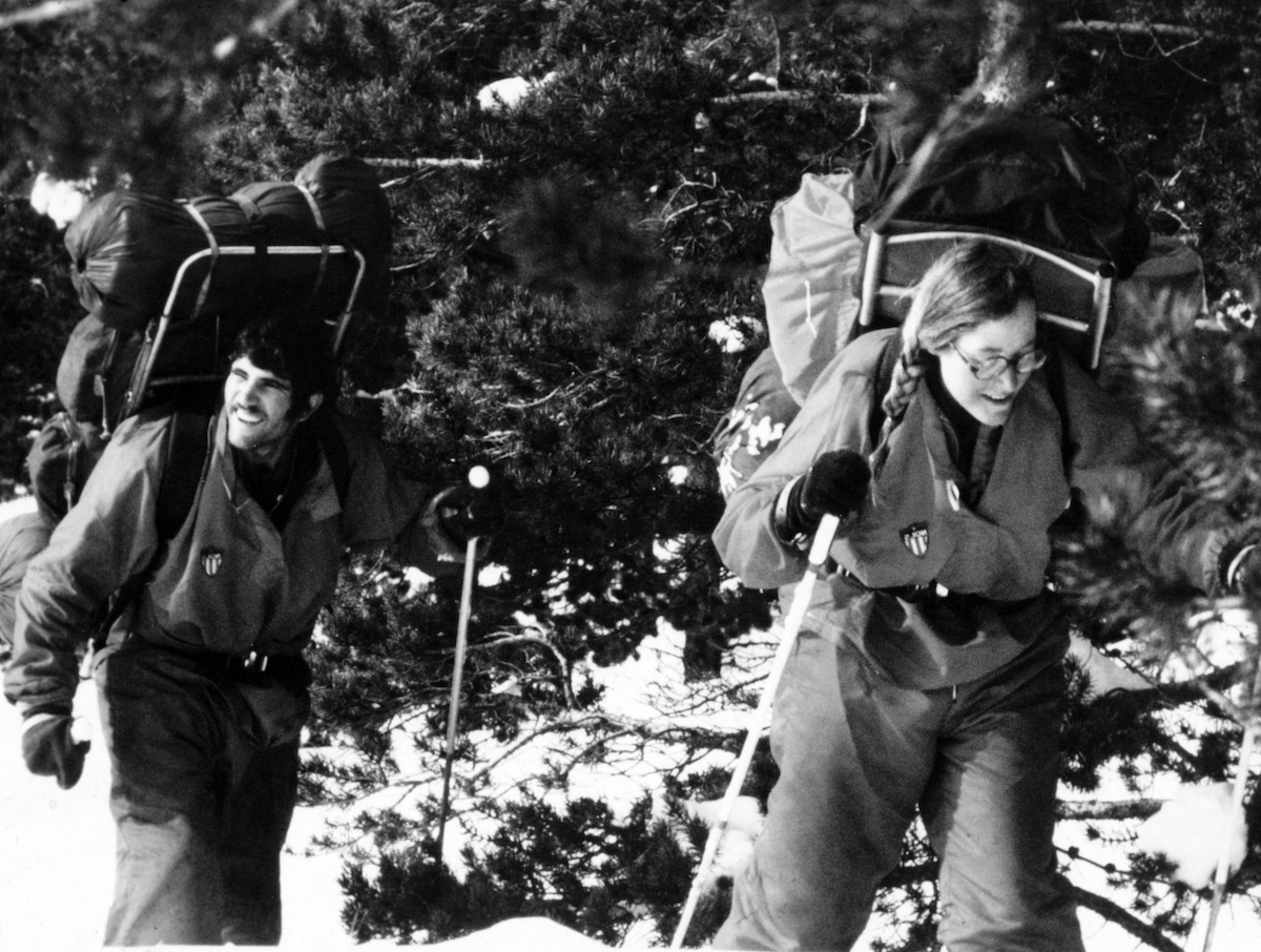 black and white photo of smiling NOLS students hiking with huge frame packs in the 1970s