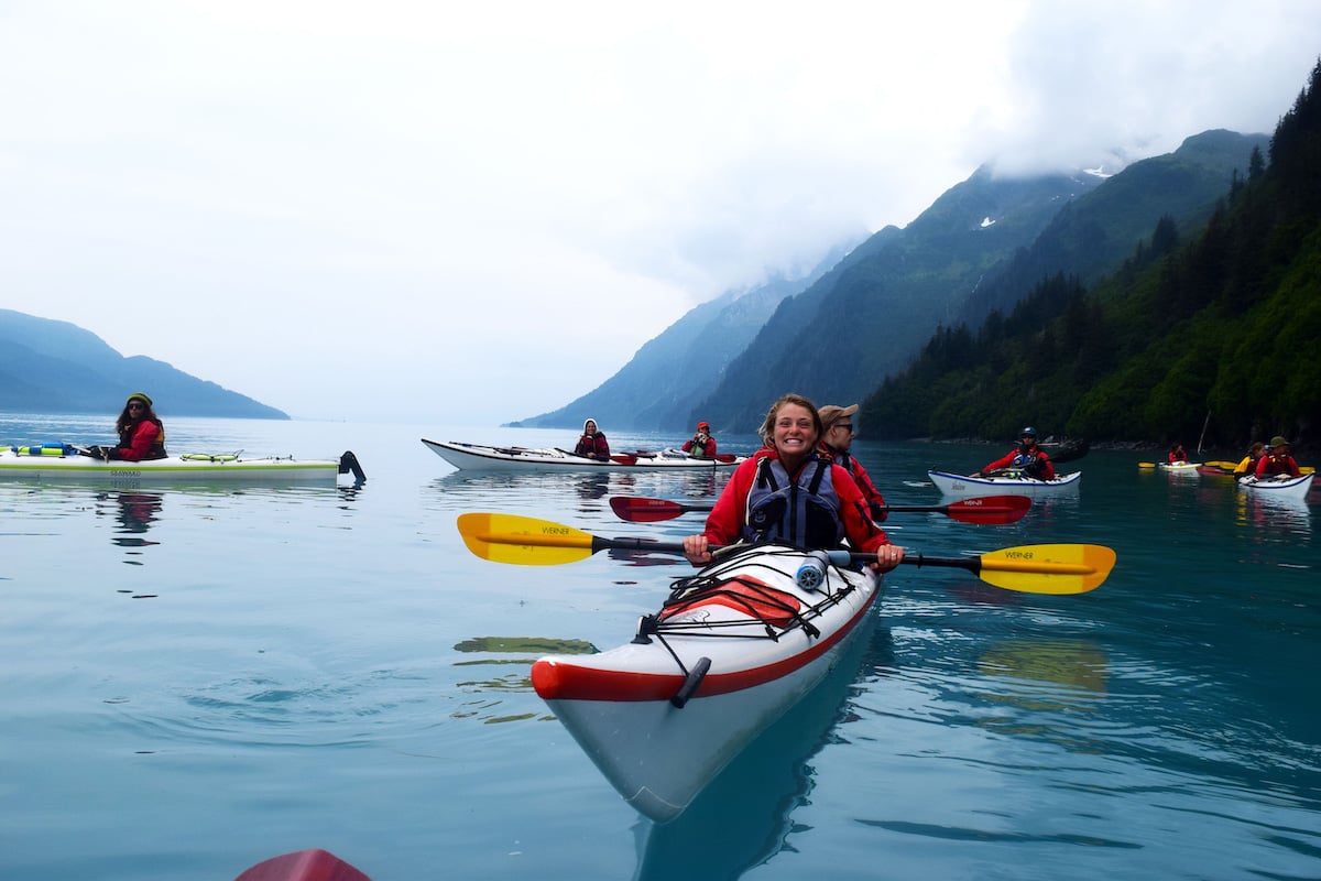 smiling NOLS students paddle single and double kayaks on calm water on a foggy day in Alaska