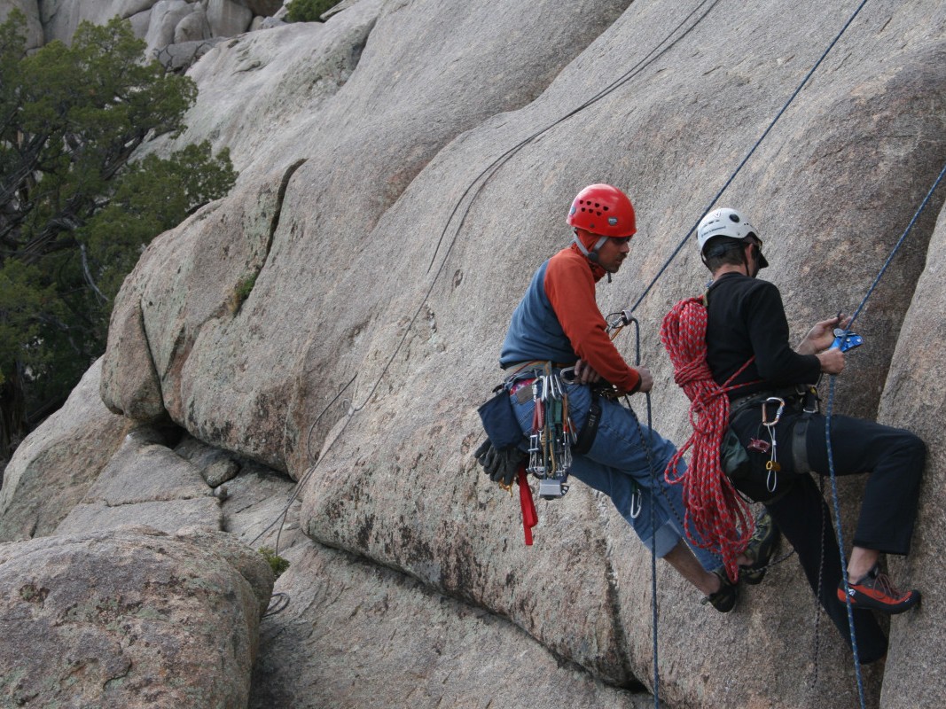 One person coaches another down a rock face
