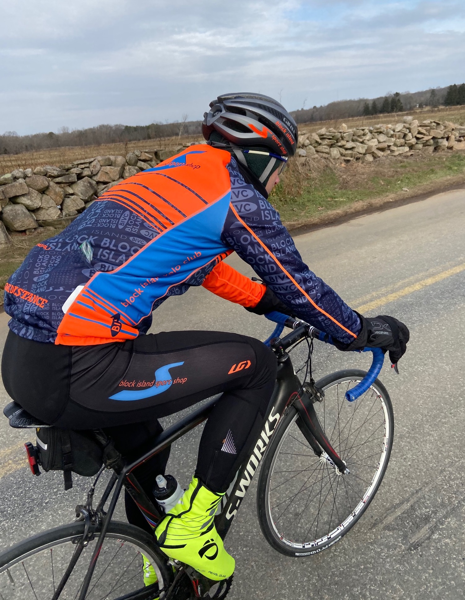 cyclist wearing blue and orange kit rides on a paved road alongside stonewall