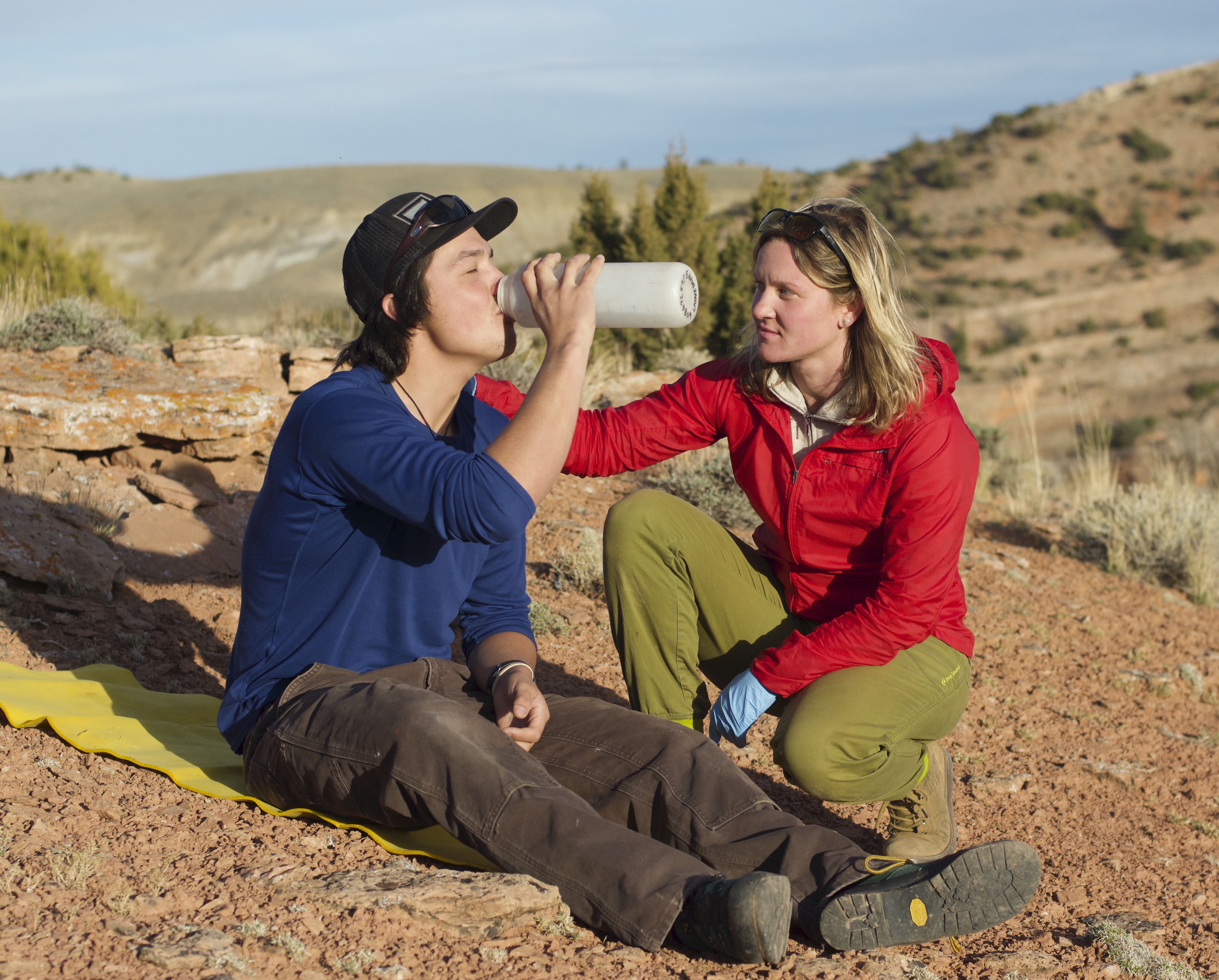 NOLS wilderness medicine participant puts a hand on the shoulder of a mock patient drinking water