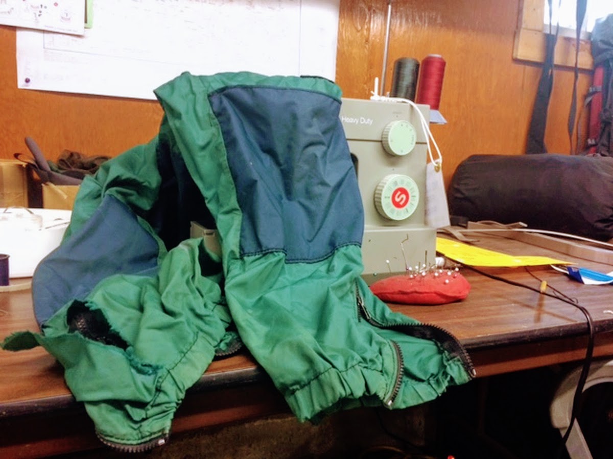 green and blue NOLS windpants draped over a sewing machine awaiting repair