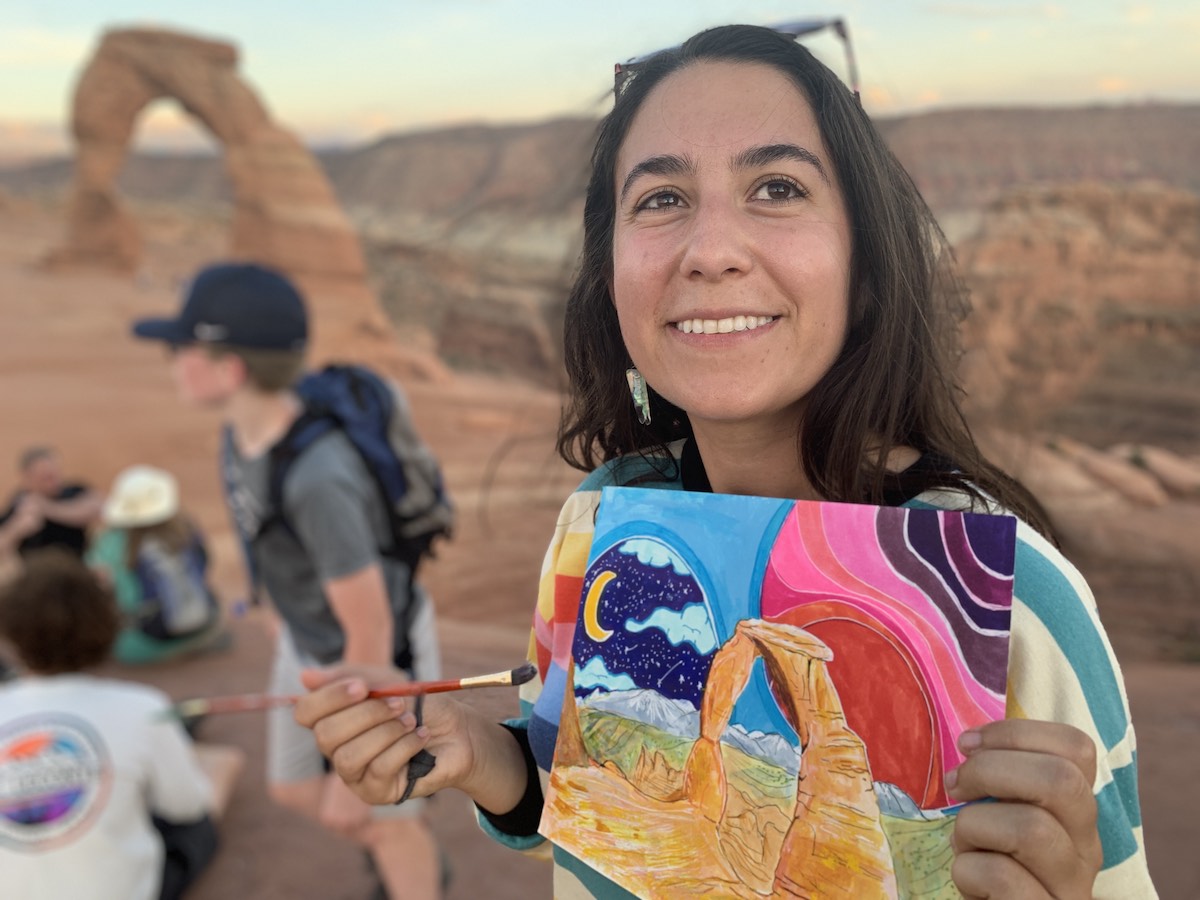 Artist smiles and holds up a painting of a redrock arch