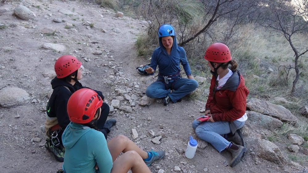 Four climbers sit together in a circle, with their helmets and gear still on, to chat