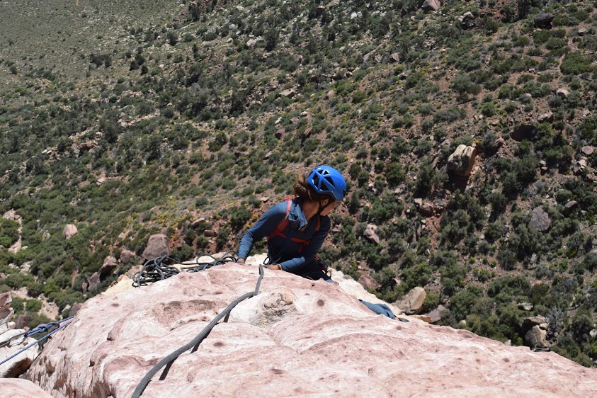 A climber wearing blue helmet glances below her from high on a rock wall