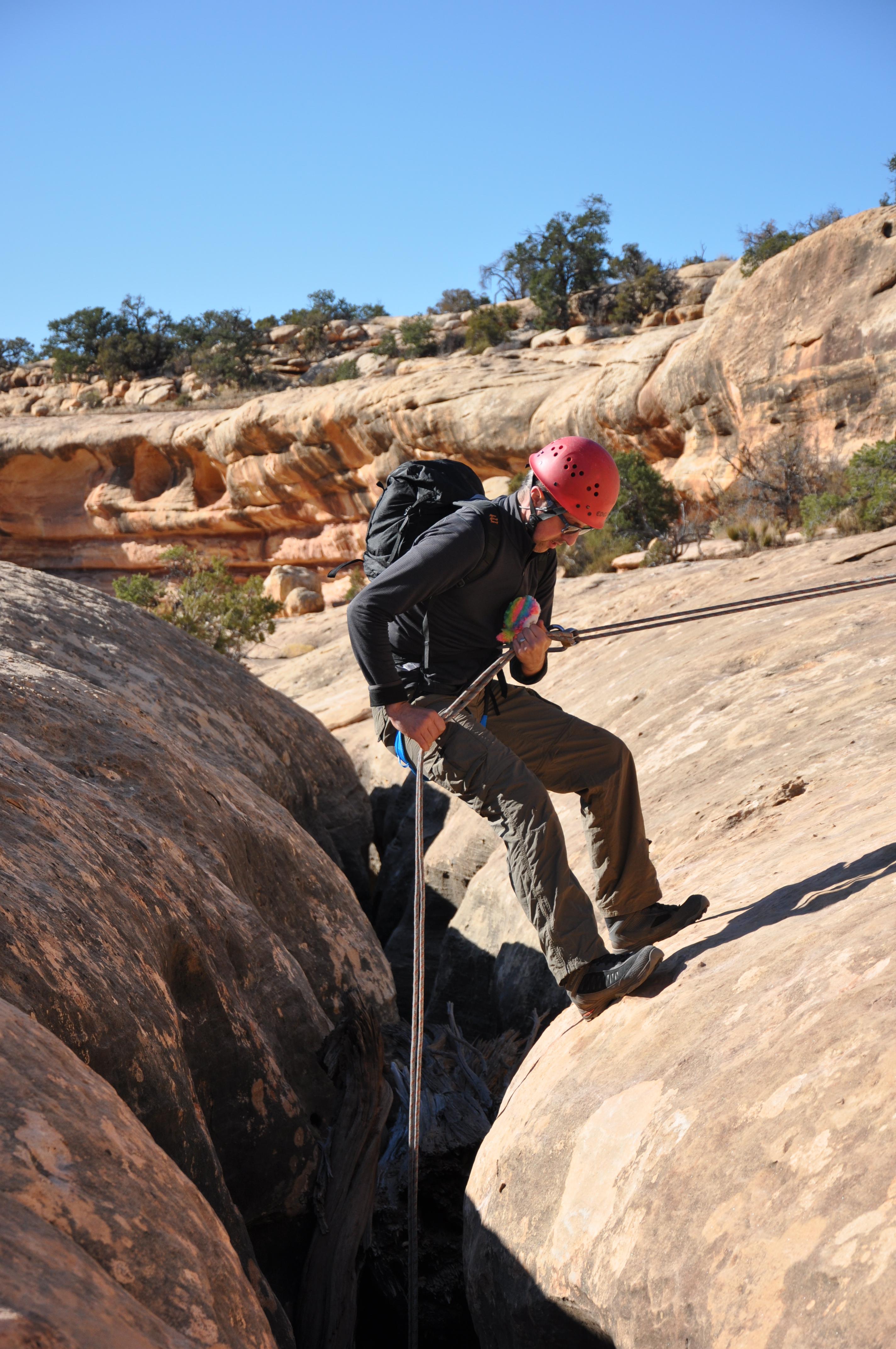 NOLS student wearing red helmet rappels in Utah's canyonlands