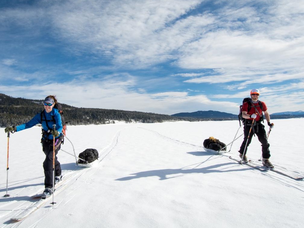 Two people smile while ski touring in a wide snowy field