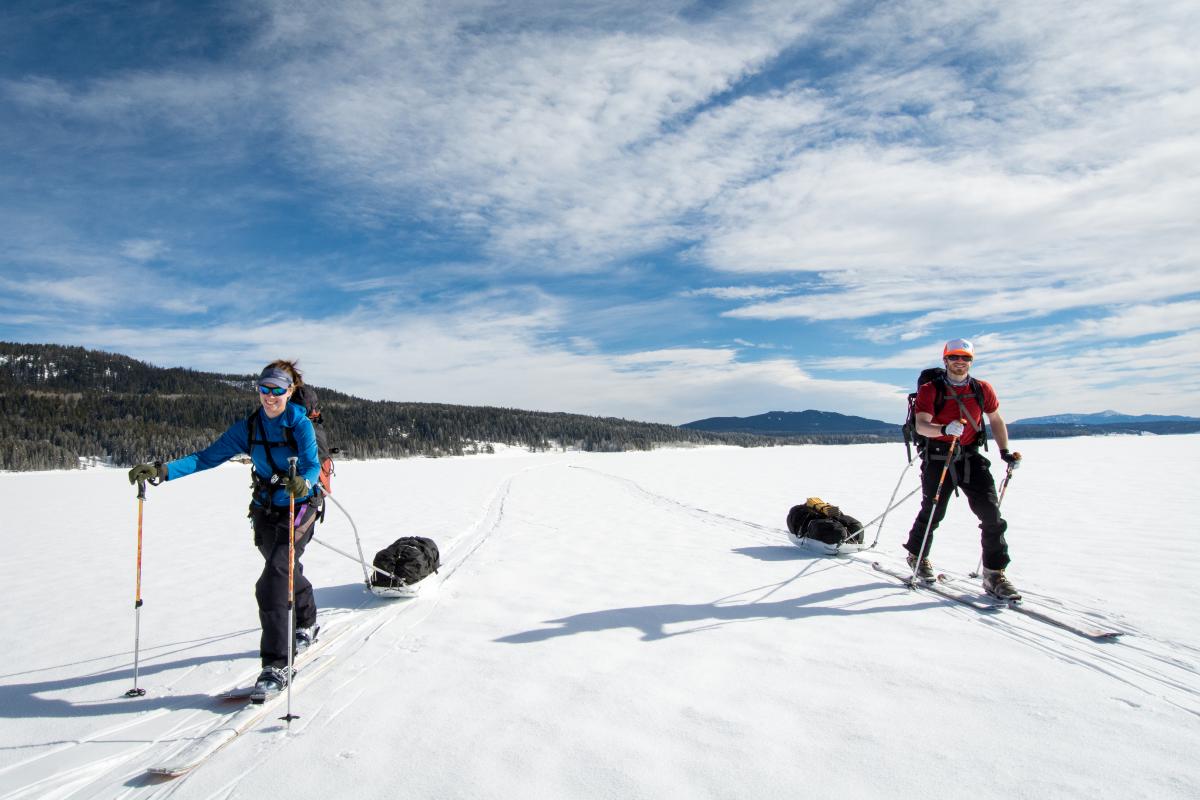 Two people skiing and pulling sleds on snow and smiling