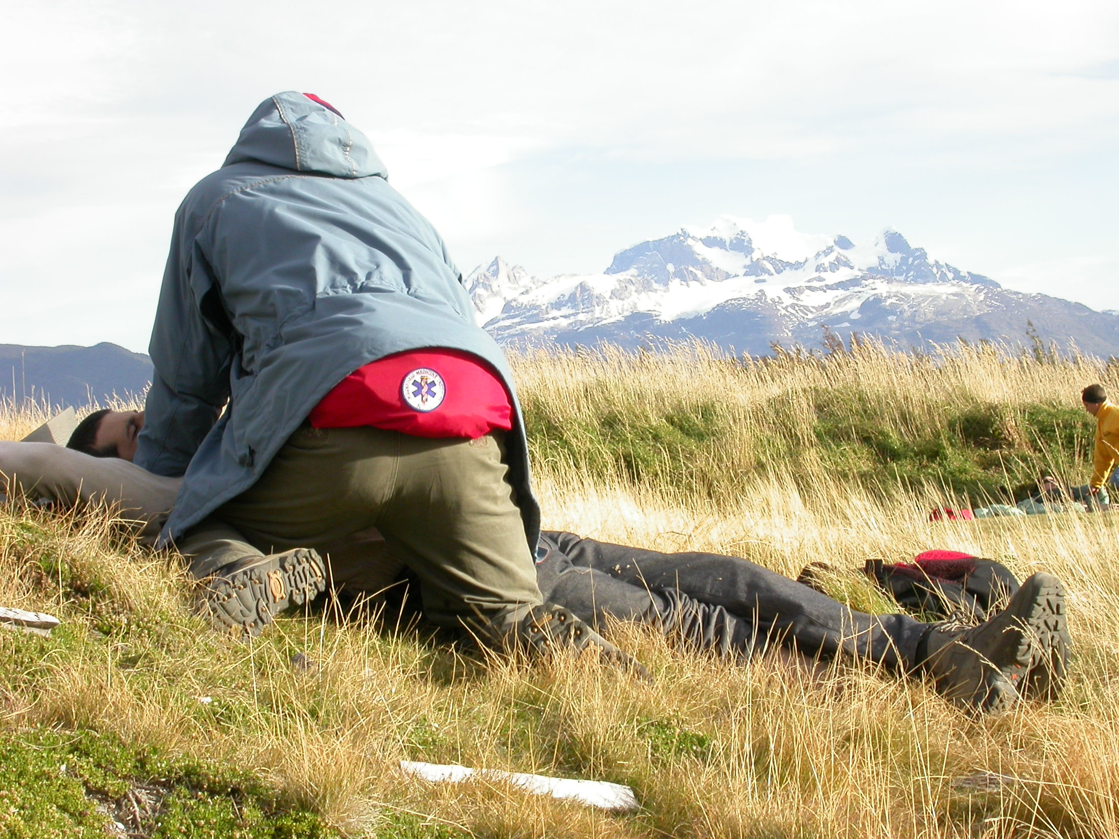 NOLS wilderness medicine student practices caring for a patient lying in the grass with a view of snow-capped mountains beyond