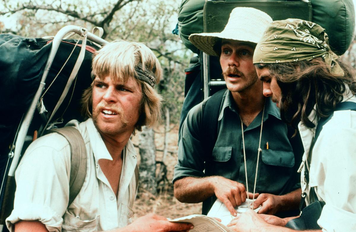 three male students with frame packs hold a map and look into the distance