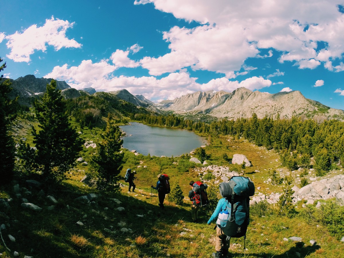 Group hikes down a hill toward an alpine lake