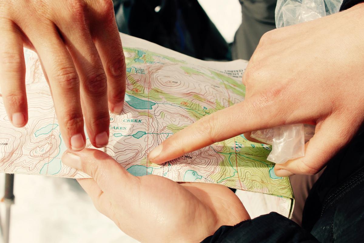 three hands holding and pointing at a topo map