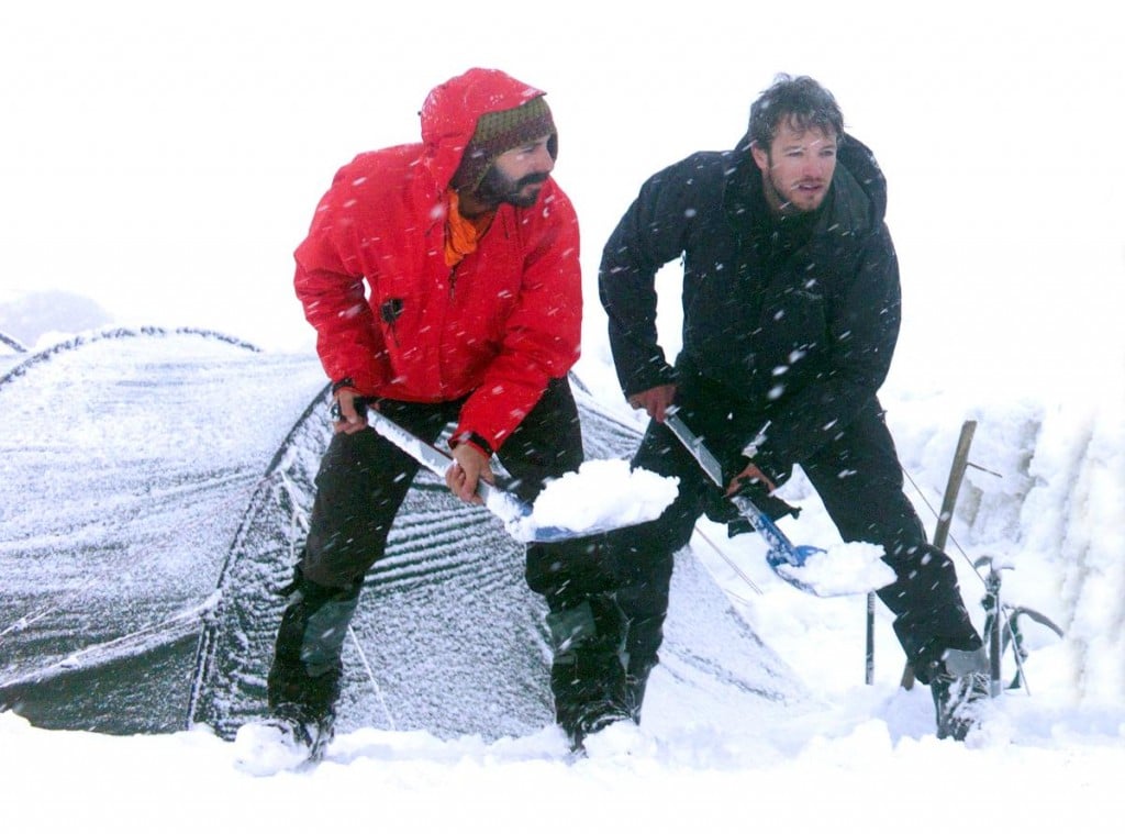 NOLS participants shovel snow outside a tent to stay warm