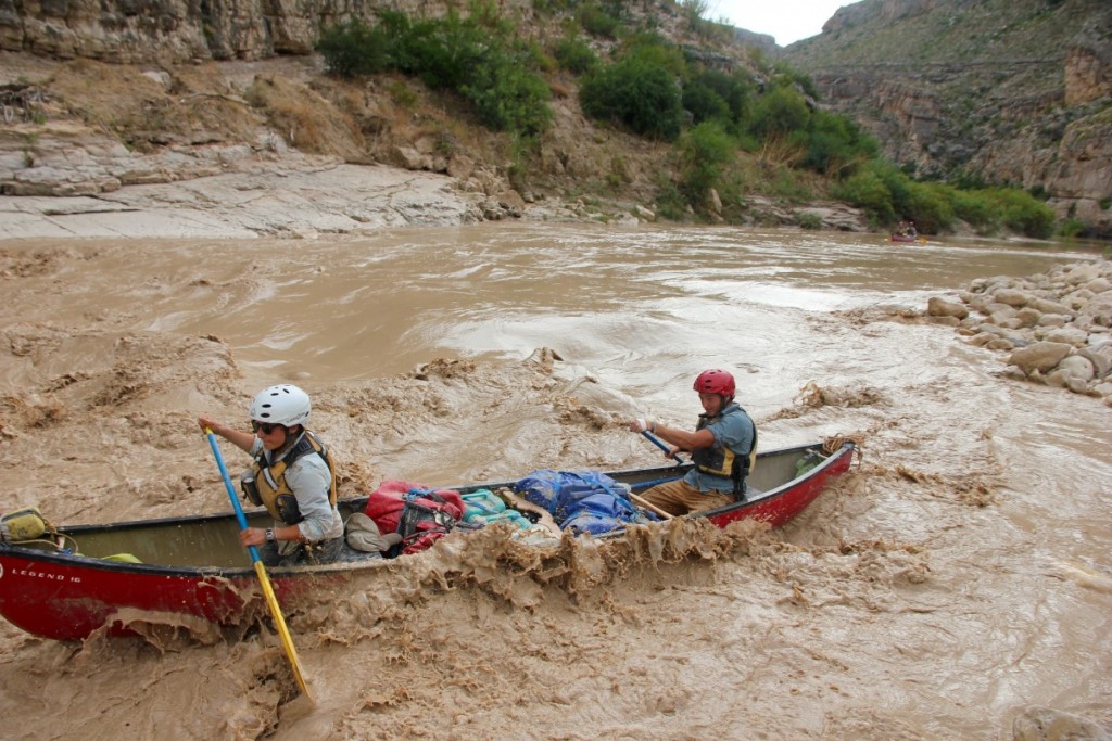 Canoeists paddle on a wide and muddy river