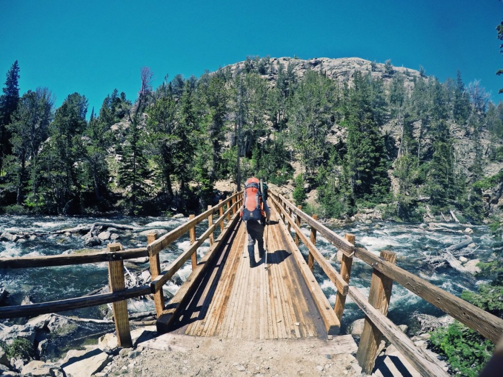 Backpackers cross a bridge over a river