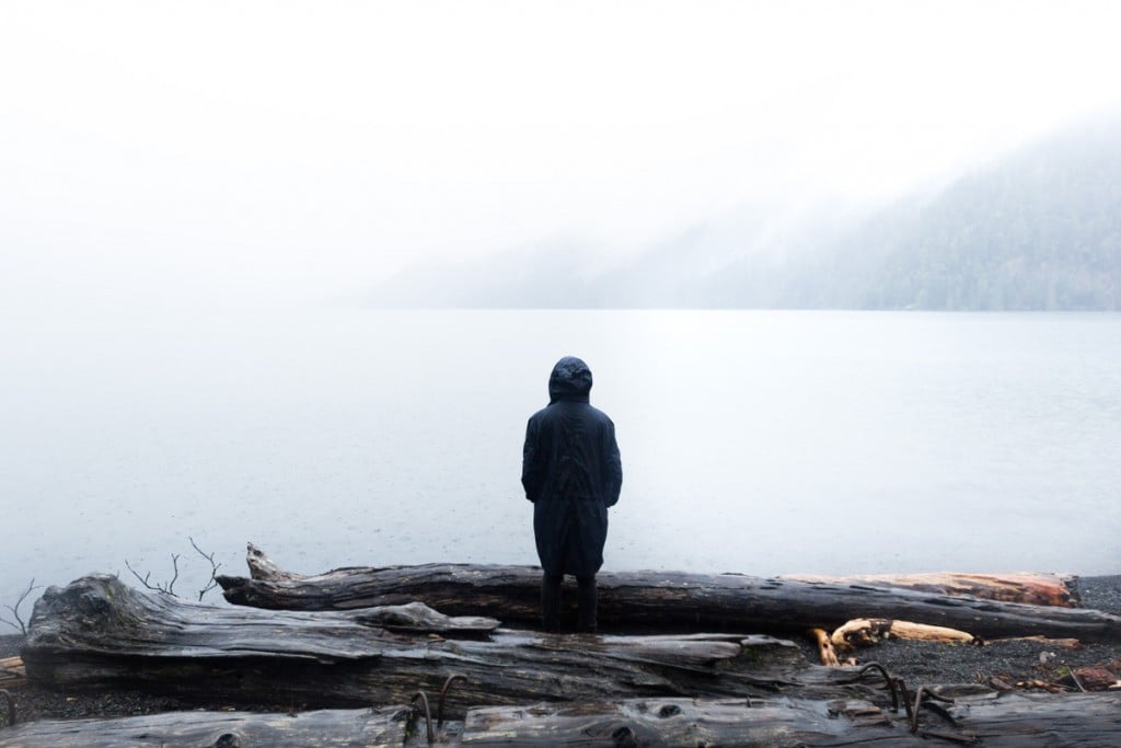 Person wearing a hooded jacket looks out on a misty lake
