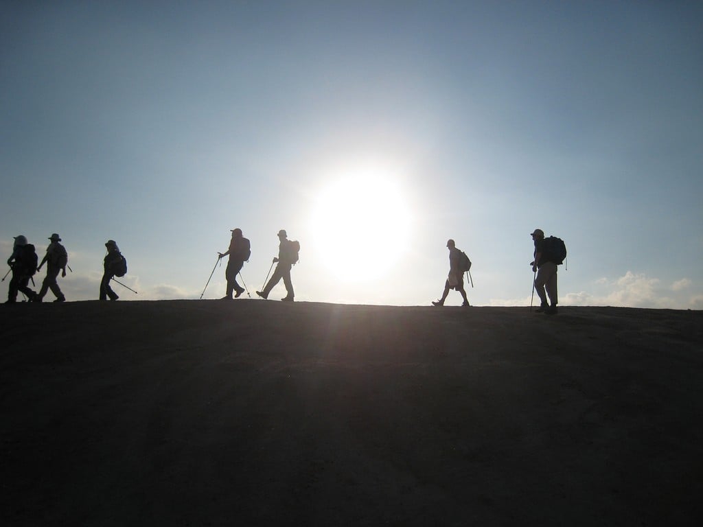 Silhouette of a line of hikers with the bright sun behind them.