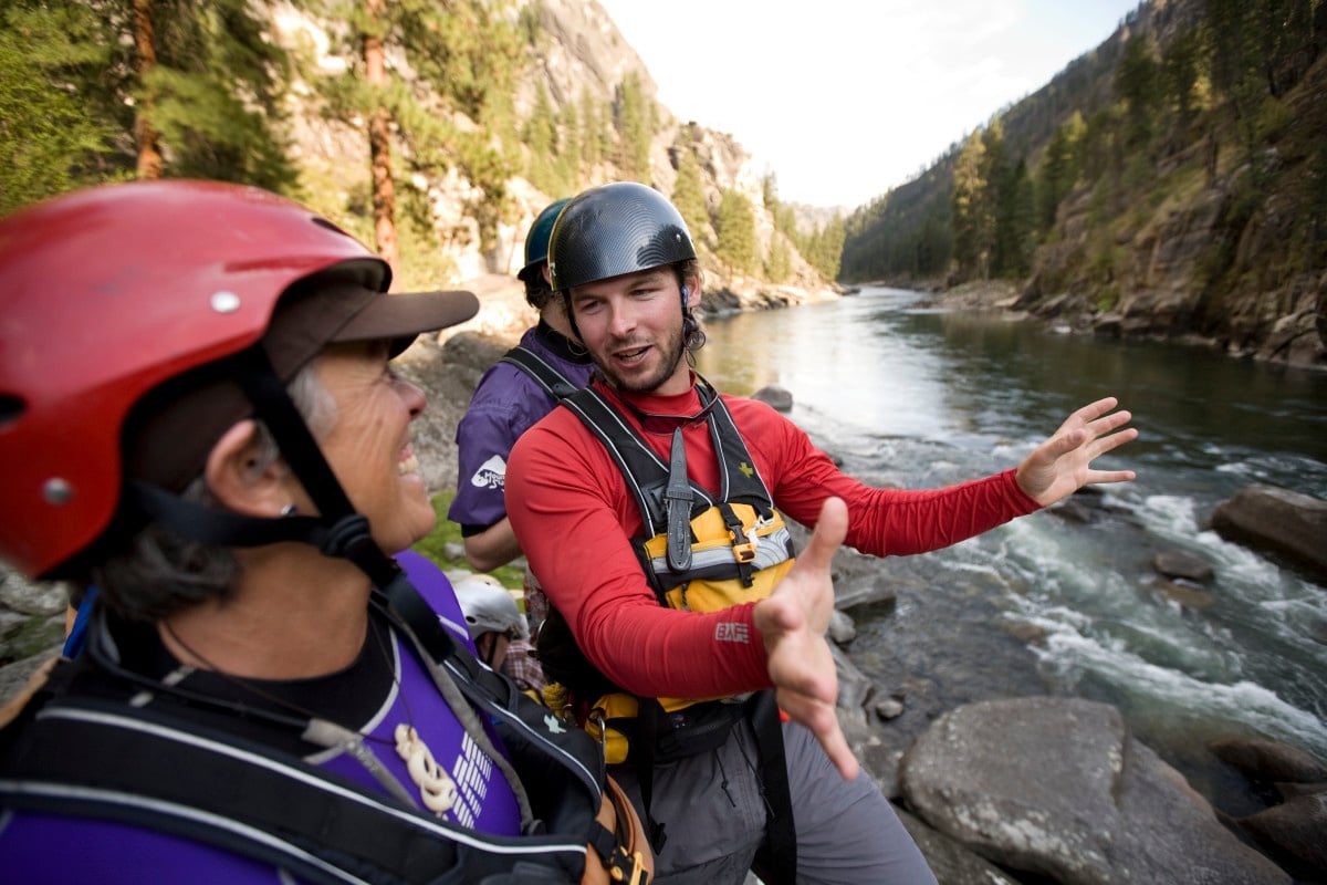 NOLS participant gestures with hands while talking with an instructor beside a river