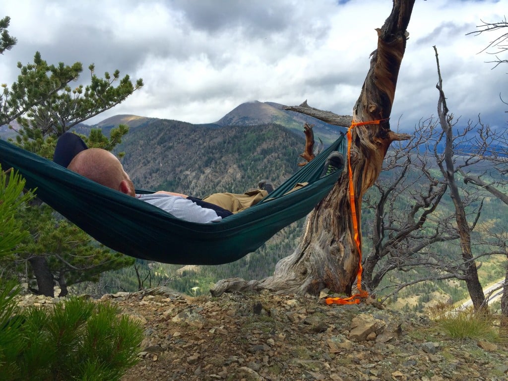 man naps in a green hammock overlooking forested mountains