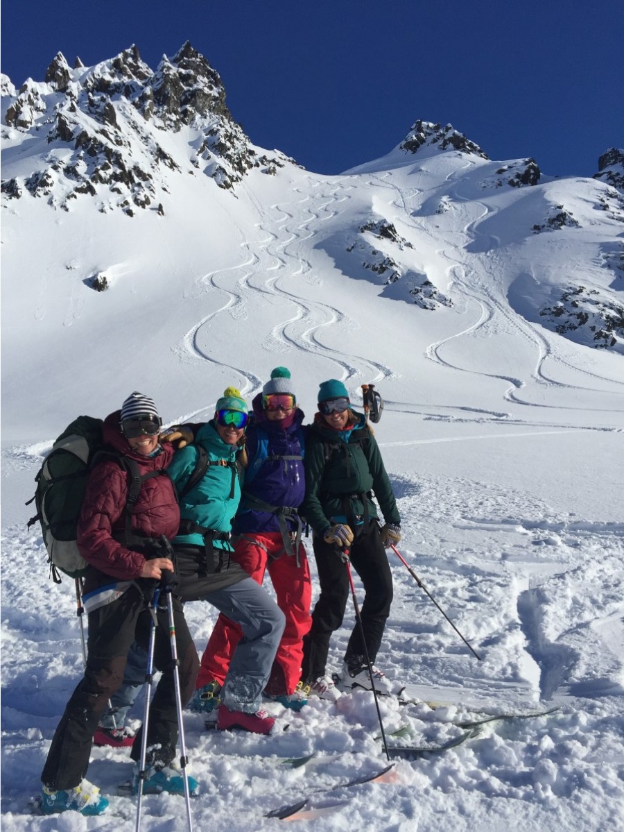 Group of four people smiling and wearing touring skis with mountains in the background