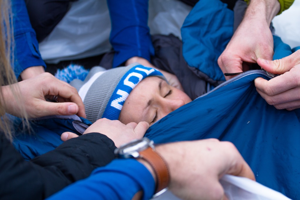 participant in a NOLS Wilderness Medicine scenario is zipped into a sleeping bag as part of treatment for hypothermia