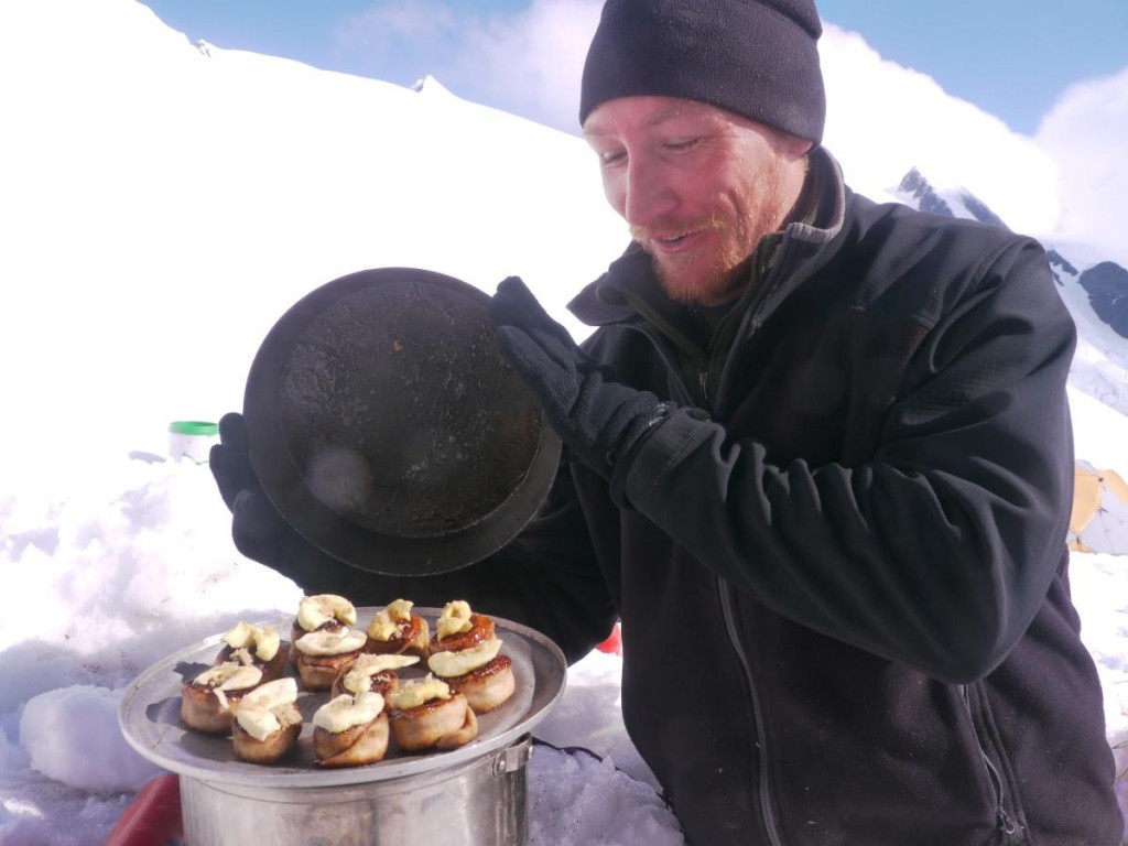 Smiling NOLS participant bakes backcountry buns in a snowy kitchen