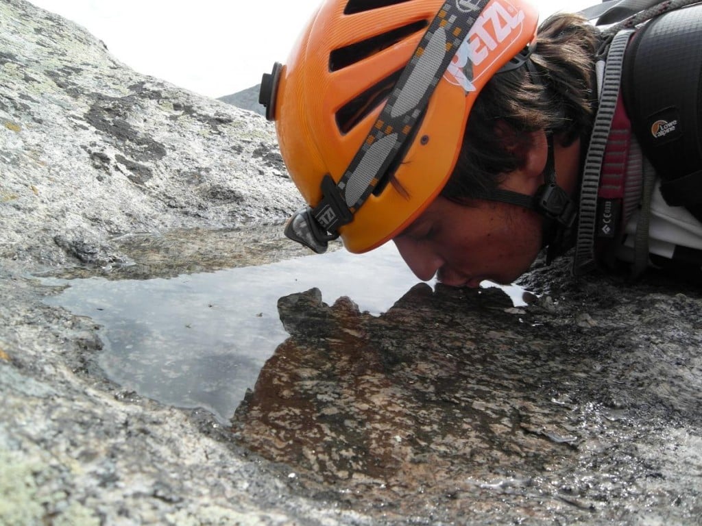 Man wearing a climbing helmet drinks water from a shallow rock depression