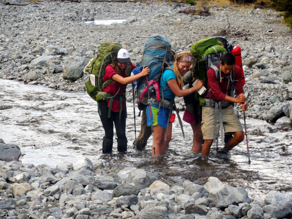 three NOLS students work together to cross a river in New Zealand