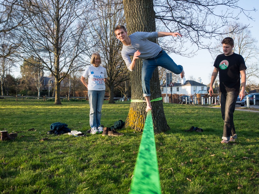 man balances on one foot on a slack line while two friends watch