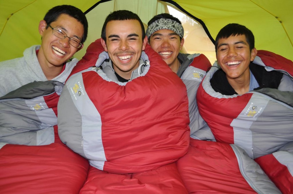 four smiling NOLS participants sit up in sleeping bags in a tent