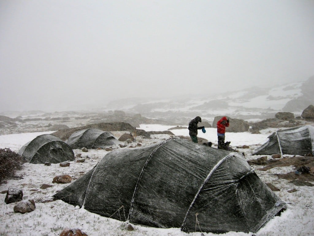 Two people in a group tentsite while it's snowing