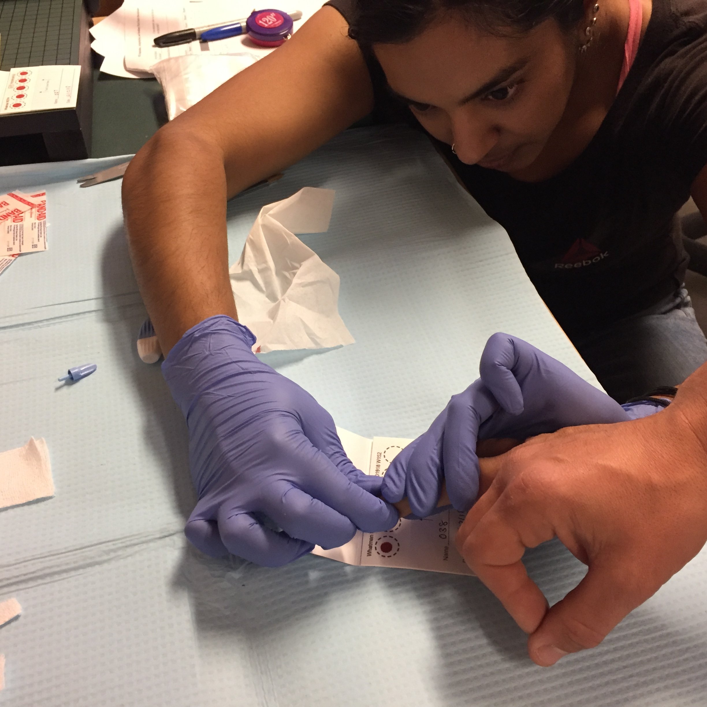 Research wearing rubber gloves collects blood sample from a NOLS student's hand