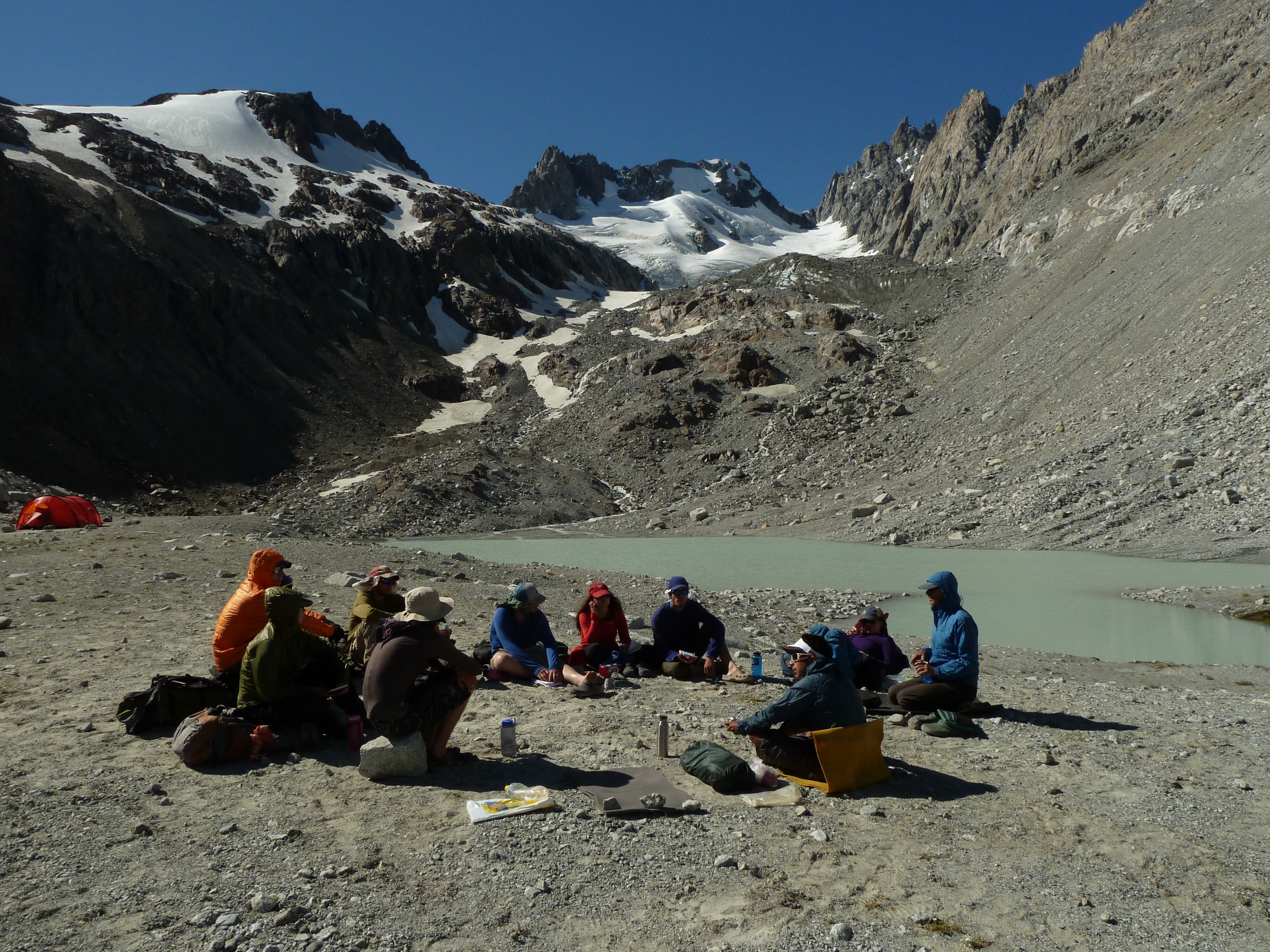 Group sits in a circle by a rocky lakeshore