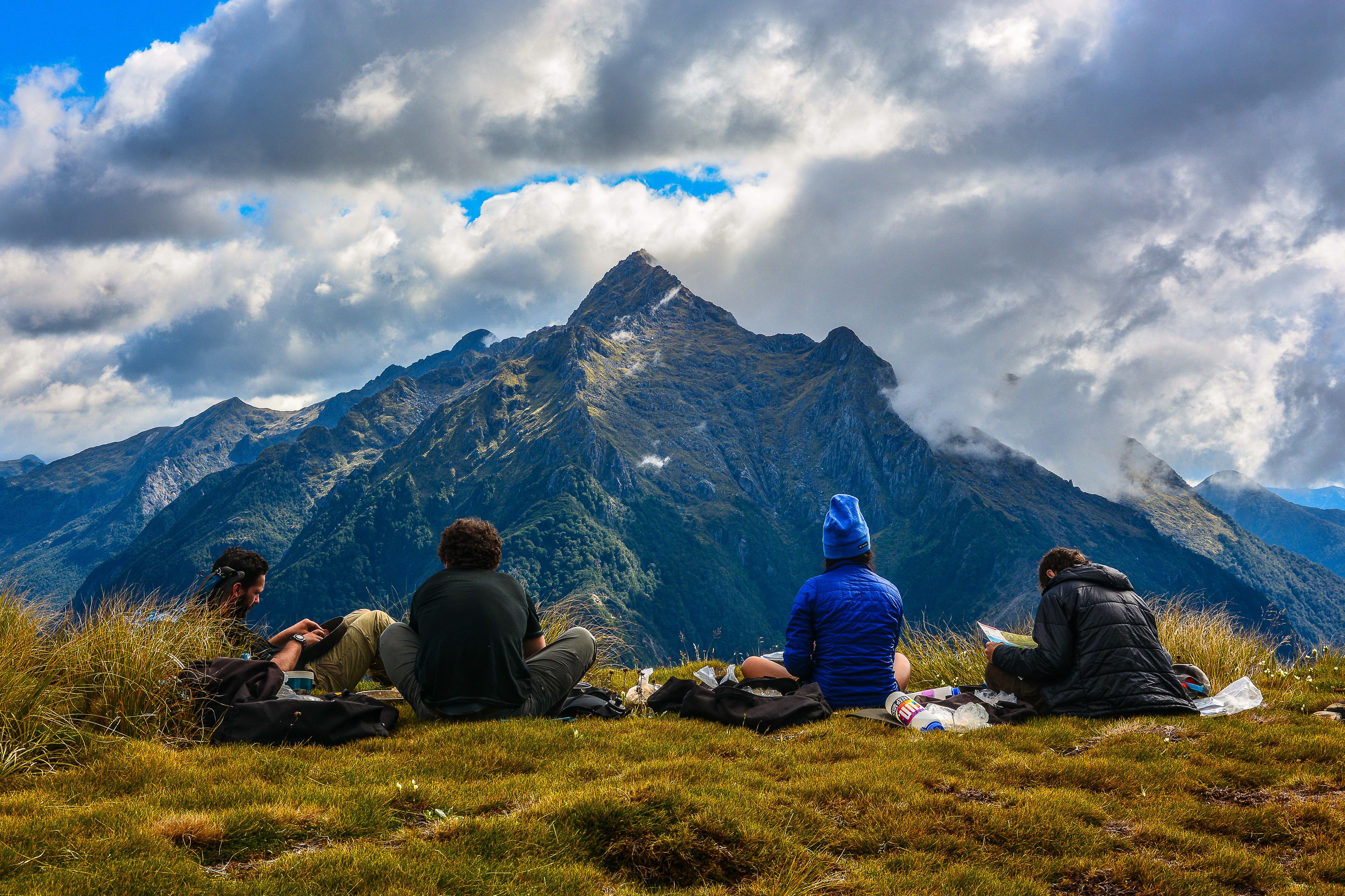 four students sit together looking out at a craggy mountain peak in New Zealand with puffy clouds overhead